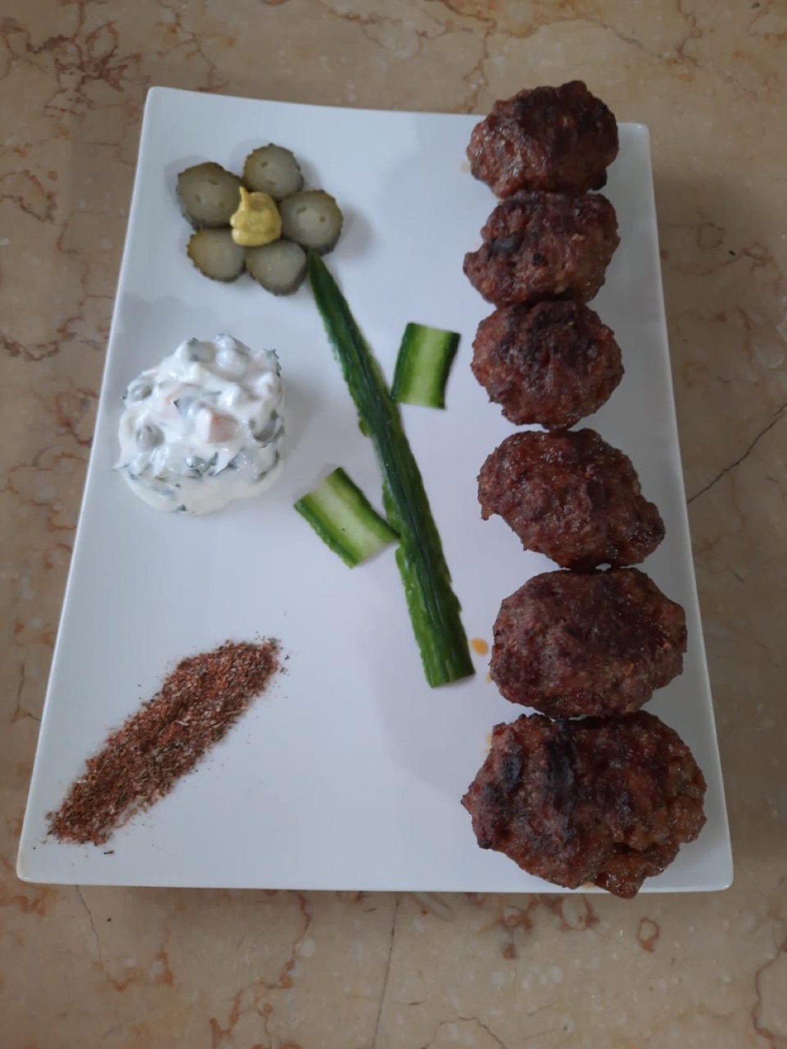 Charcoal-grilled meatballs plated with pickles and yogurt
