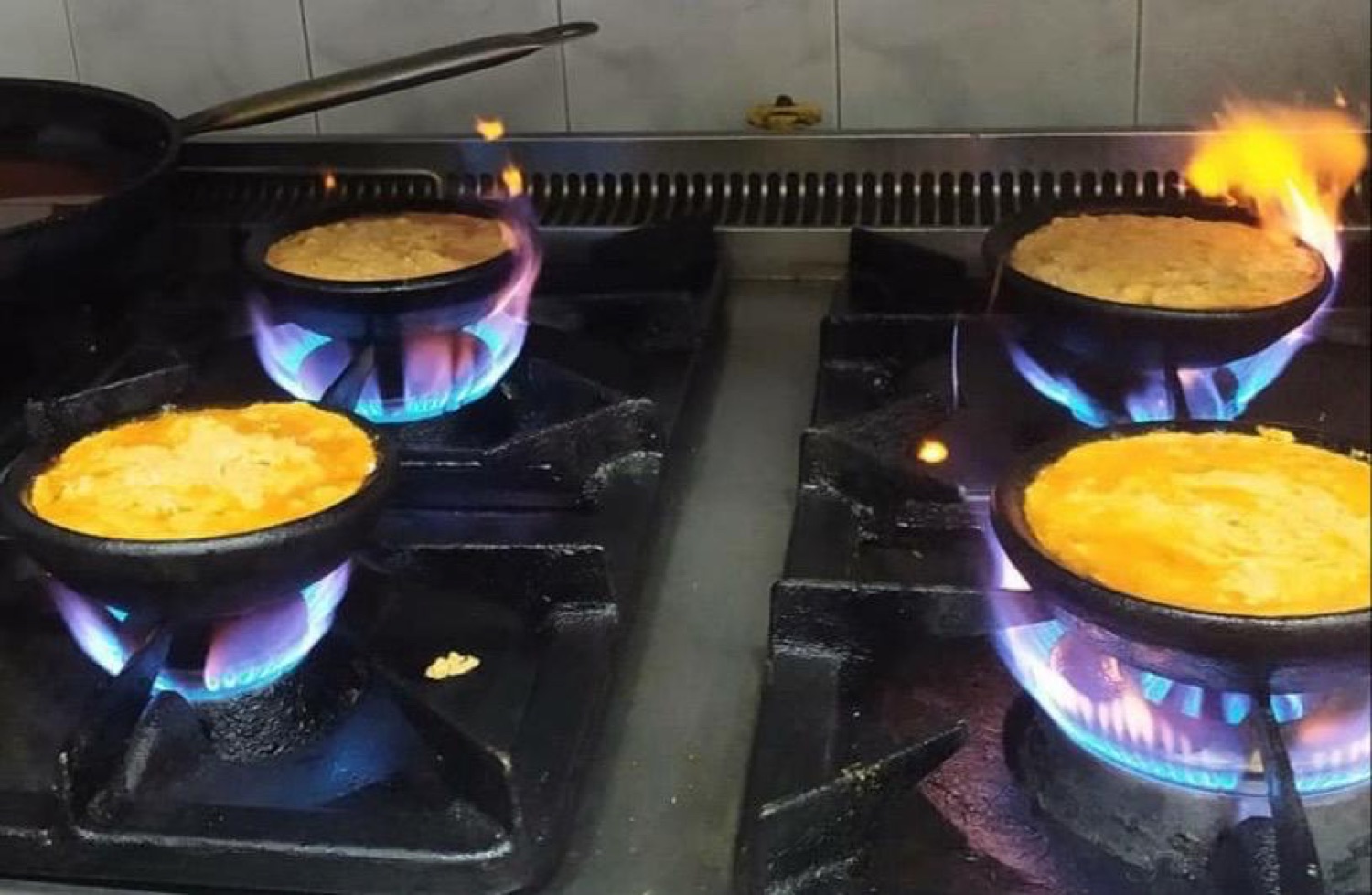 Fërgesë bubbling in clay pots over a blue gas flame